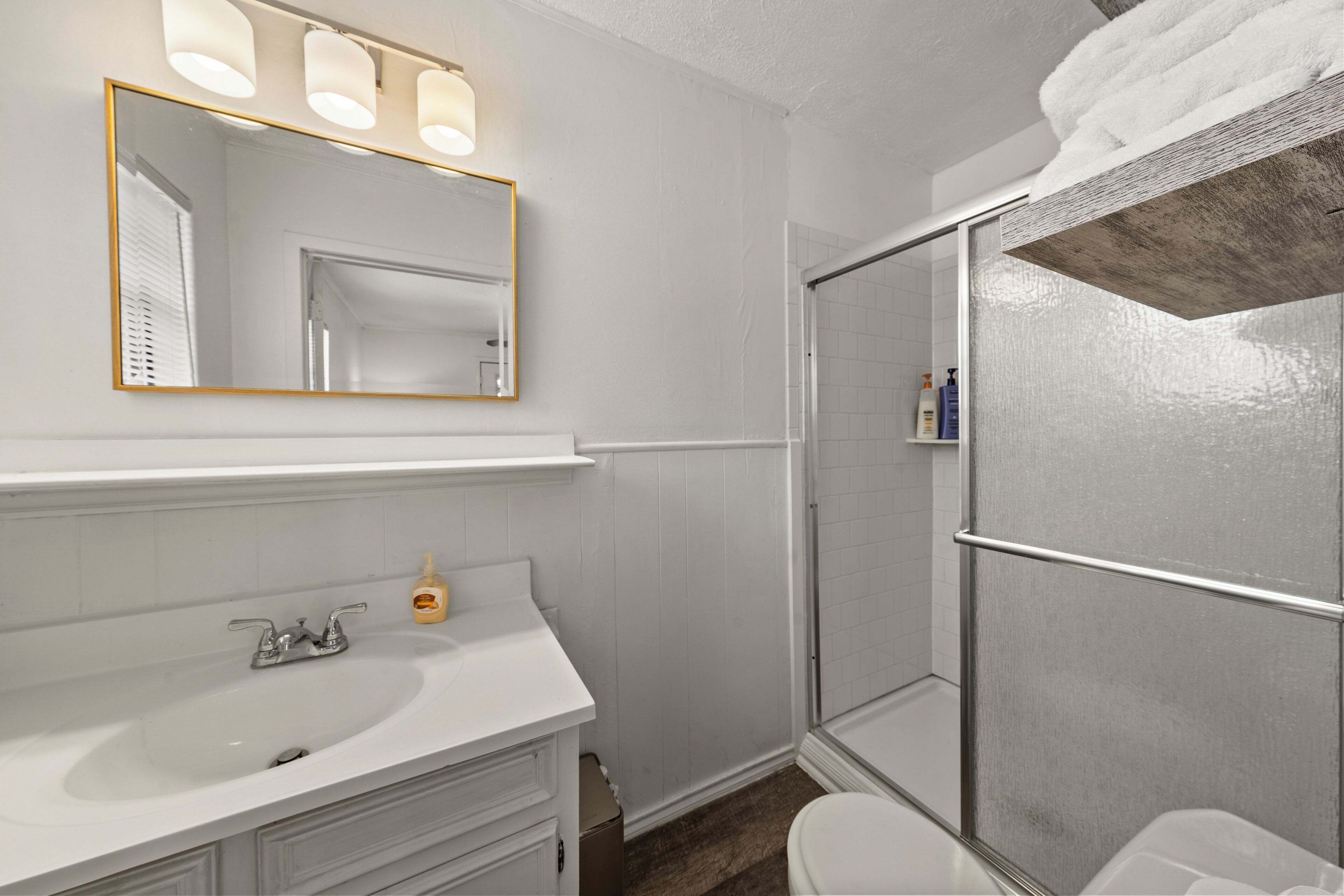 Een badkamer met een witte wastafel, een spiegel met verlichting, een douche met glazen deur en een toilet.