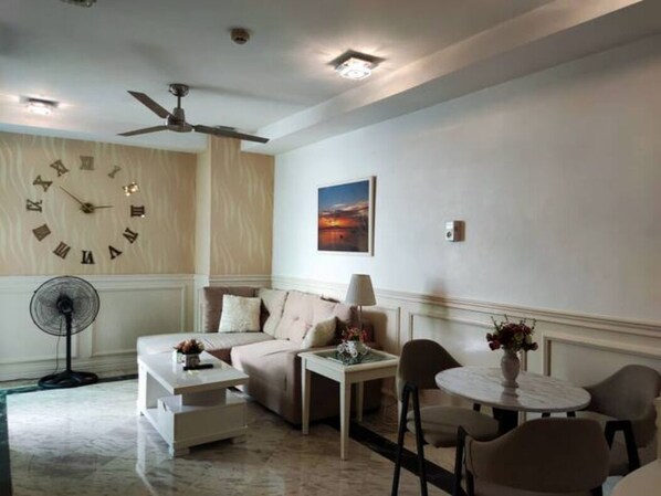 A living room with a ceiling fan, a clock, a sofa, a coffee table, a side table, and a dining area with chairs and a table. - air-conditioned condo with balcony and bay view in malate, manila (City Of Manila)