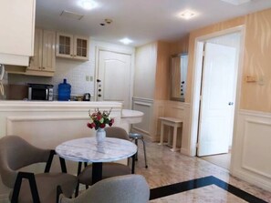 A kitchen with white cabinets, a blue water dispenser, and a round table with chairs. - air-conditioned condo with balcony and bay view in malate, manila (City Of Manila)