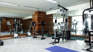Een sportschool met diverse fitnessapparaten, een grote spiegel en een blauwe mat op de vloer.