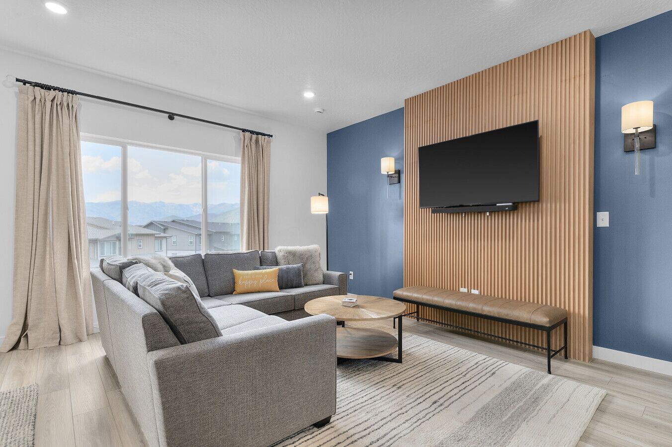 A modern living room with a grey sectional sofa, a round coffee table, and a TV mounted on a wooden wall.
