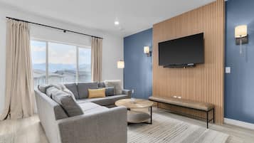 A modern living room with a grey sectional sofa, a round coffee table, and a TV mounted on a wooden wall.