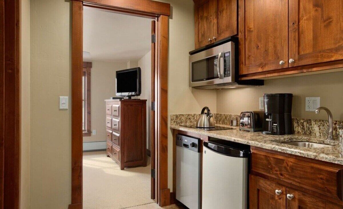 A compact kitchen with wooden cabinets, a microwave, a coffee maker, and a dishwasher.