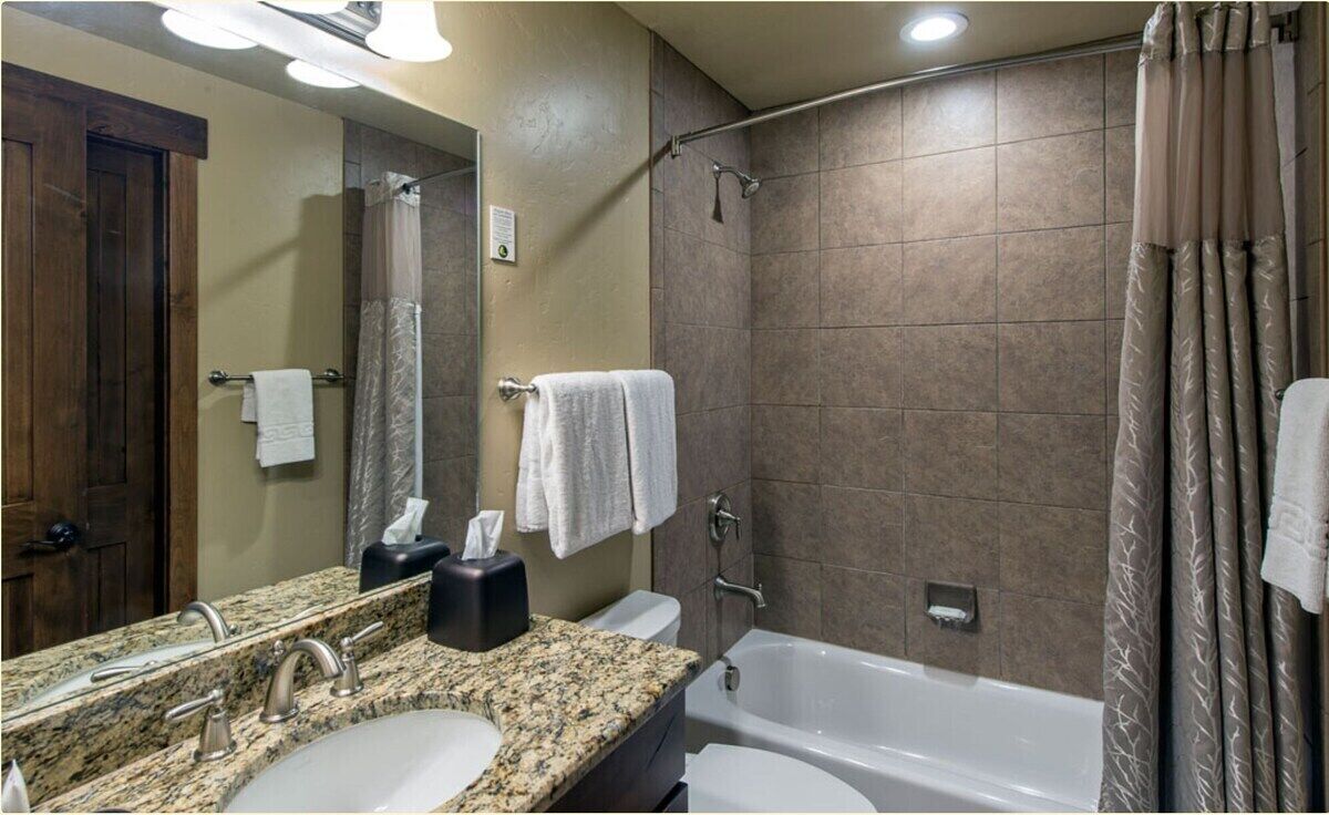 A bathroom with a granite countertop sink, a mirror, a bathtub, and a shower curtain.