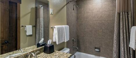 A bathroom with a granite countertop sink, a mirror, a bathtub, and a shower curtain.