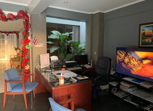 A modern office with a desk, computer, and a large TV screen. There are chairs, a plant, and a window with curtains. - Stada (Alajuela)