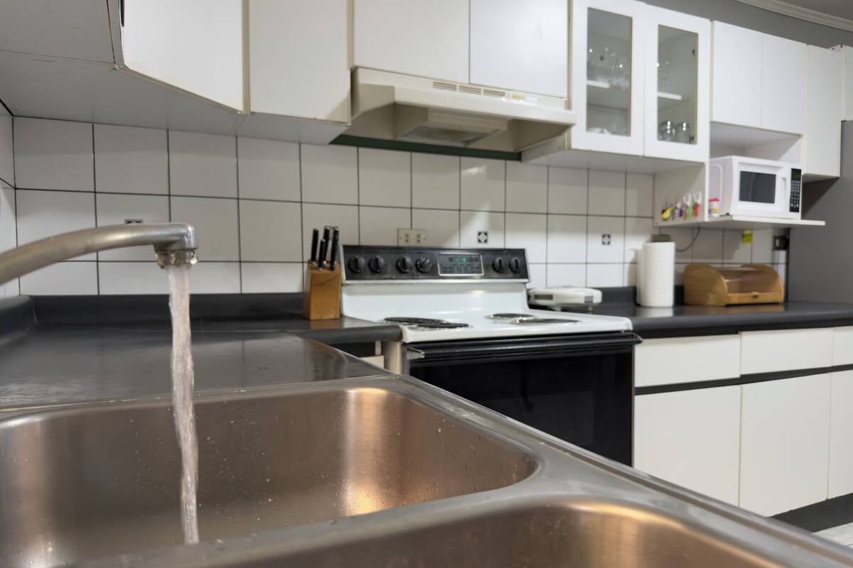 A kitchen with a stainless steel sink, a stove, and white cabinets.