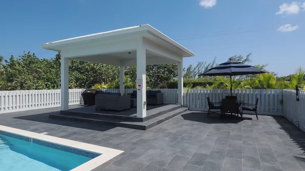 Un'area esterna coperta con piscina, sedute e un pergolato.