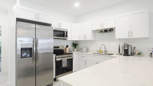 Una cucina moderna con mobili bianchi, elettrodomestici in acciaio inossidabile, forno integrato e una grande isola con lavello.