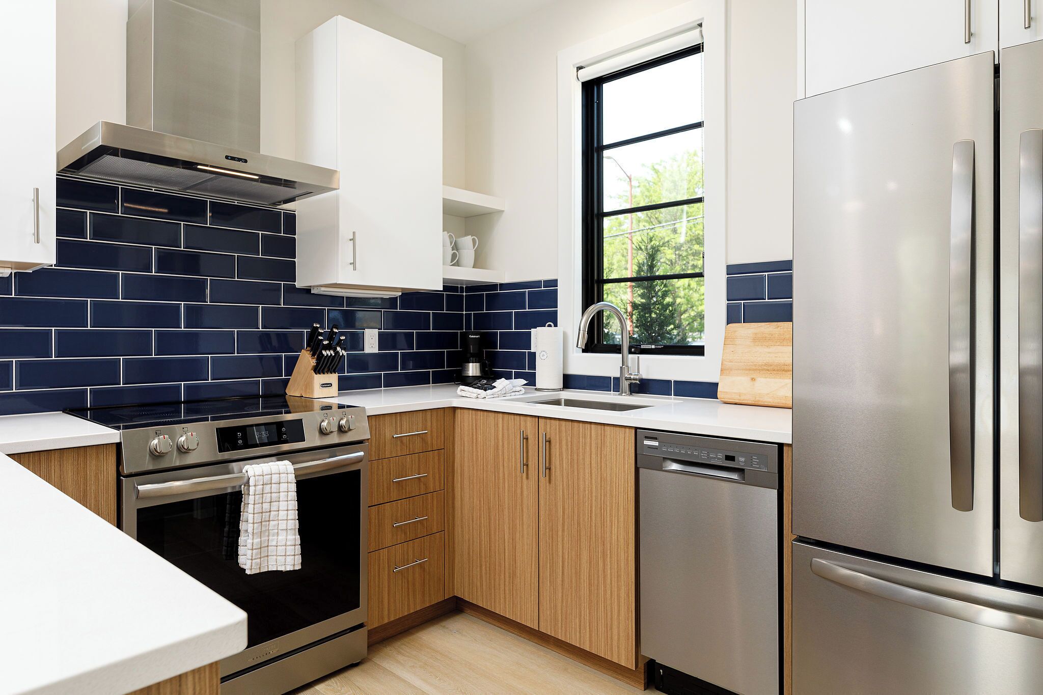 A modern kitchen with stainless steel appliances, wooden cabinets, and a blue-tiled backsplash.