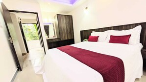 A modern hotel room with a large bed, a wooden headboard, and a view of greenery outside.