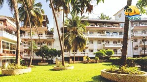 A multi-story hotel with a lush garden, palm trees, and a clear sky.
