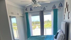 A bedroom with a bed, a sofa, a ceiling fan, and a view of the outdoors.