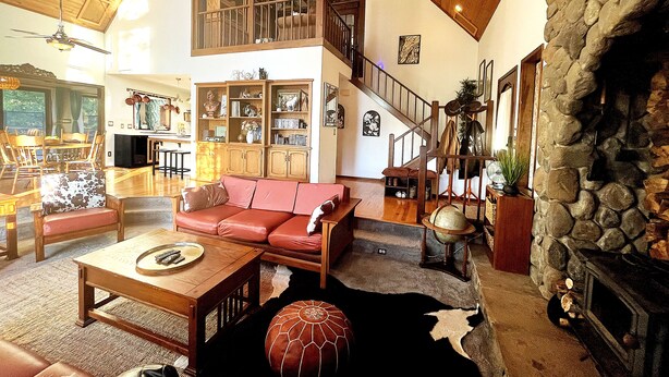 A spacious living area with a high ceiling, a fireplace, a staircase, and a large bookshelf. - "Stunning Views" • "Very Private" • "Coziest Beds" • Foxfell At Shasta Lake (Lakehead)