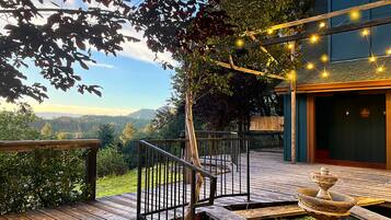 A wooden deck with a metal railing, a stone fountain, and string lights.