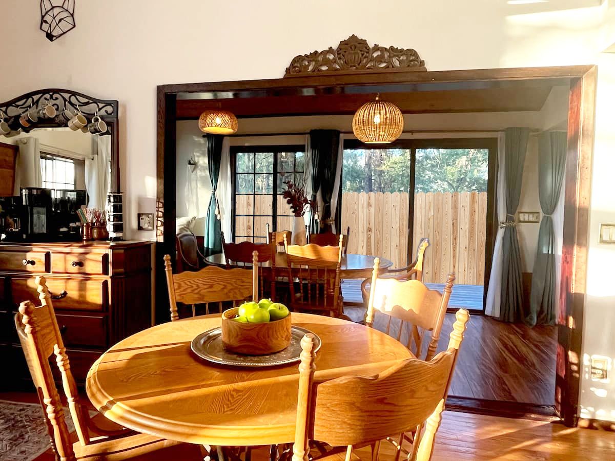 Un coin repas avec une table et des chaises en bois, un panier de fruits et une vue sur l’extérieur.