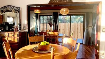 Un coin repas avec une table et des chaises en bois, un panier de fruits et une vue sur l’extérieur.