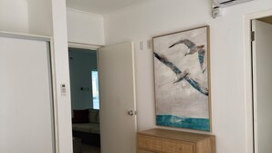 Un dormitorio con cama, ventilador de techo, aire acondicionado montado en la pared, una puerta y un cuadro.