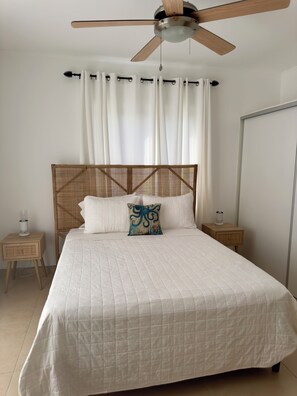 A bedroom with a bed, a ceiling fan, a nightstand, and a wall-mounted mirror.