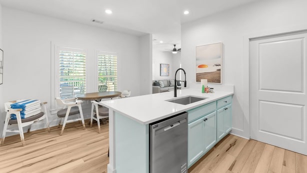 A modern kitchen with white cabinetry, a built-in dishwasher, and a dining area with a table and chairs. - Remodeled West 30A 2BR Cottage: Golf Cart, Bikes & Private Deck (Santa Rosa Beach)