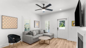 A modern living room with a grey sectional sofa, a black armchair, a round coffee table, and a ceiling fan. - Remodeled West 30A 2BR Cottage: Golf Cart, Bikes & Private Deck (Santa Rosa Beach)