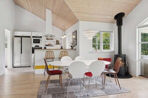 Een moderne keuken met inbouwapparatuur, een eetgedeelte met een witte tafel en stoelen, en een houtkachel.