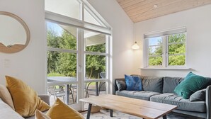 Un salon moderne avec un canapé, une table basse et de grandes fenêtres donnant sur un paysage verdoyant.