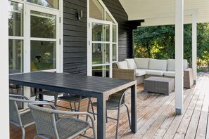 An outdoor patio with a table and chairs, a sofa, and a covered area with a view of greenery. - Holiday home with spa near beach and nature (Dannemare)