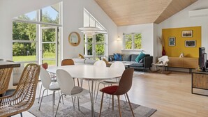 Un vaste espace de vie comprenant une table à manger, des chaises, un canapé et un mur d’accent jaune.