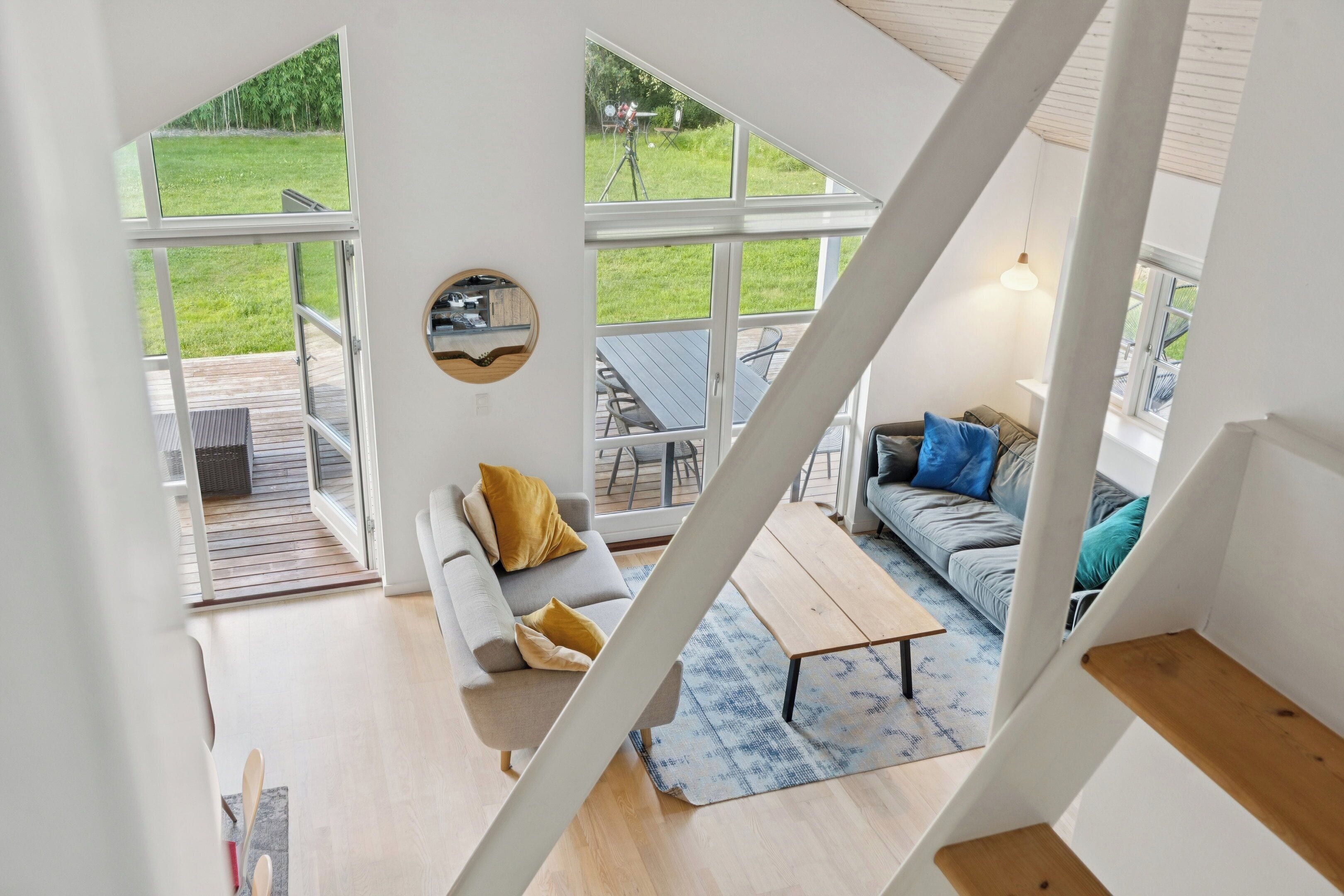 Et moderne interiør med trappe, sofa, sofabord og udsigt til en grøn have.