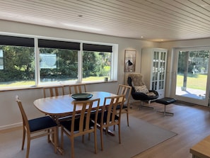 Un coin repas avec une table et des chaises, un fauteuil recouvert d’un plaid en fourrure, et une vue sur l’extérieur grâce à de grandes fenêtres.