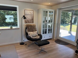 A room with a black leather chair, a white cabinet with glass doors, a framed picture on the wall, and a view of the outdoors through a large window.