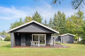 A small, dark-colored cabin with a patio area, a sliding glass door entrance, and a deck.