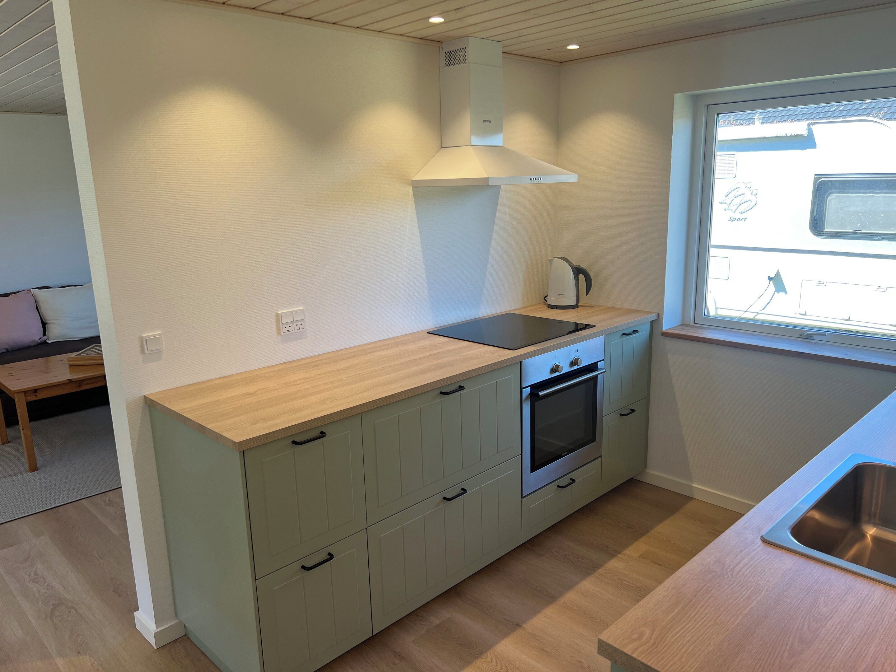 A compact kitchen with a built-in oven, a kettle, and a window with a view.