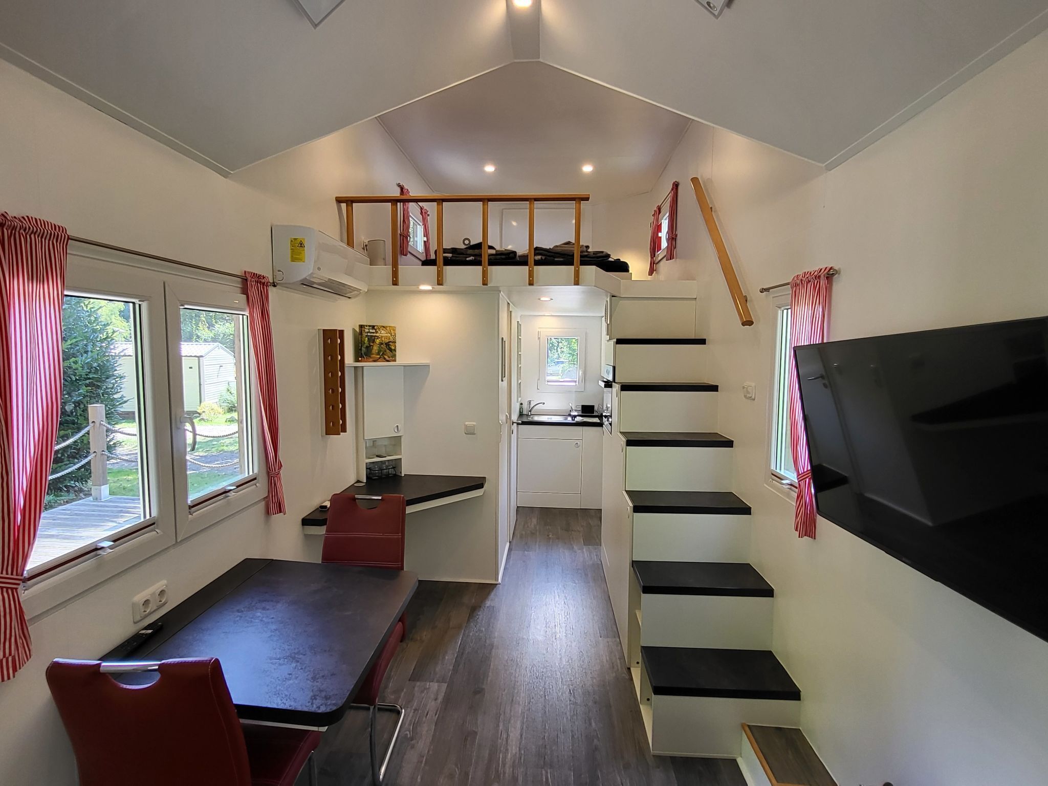A compact living space with a dining area, a kitchen, and a TV mounted on the wall.
