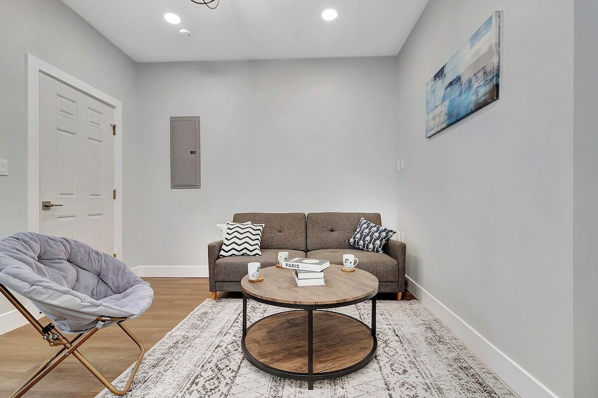 A modern living room with a grey chair, a round coffee table, a grey sofa, and a white door.