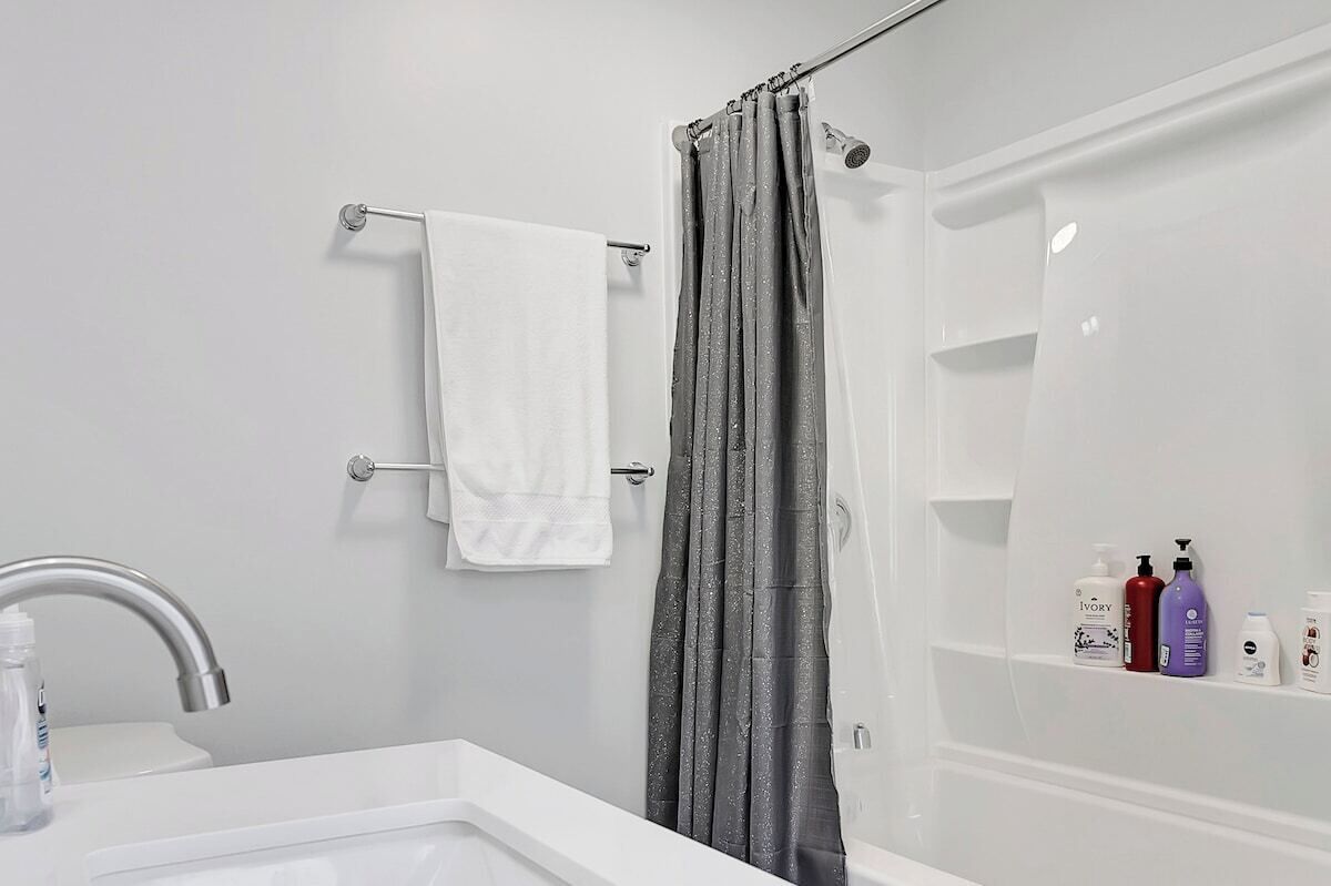 A bathroom with a white sink, a shower curtain, and a shelf with toiletries.