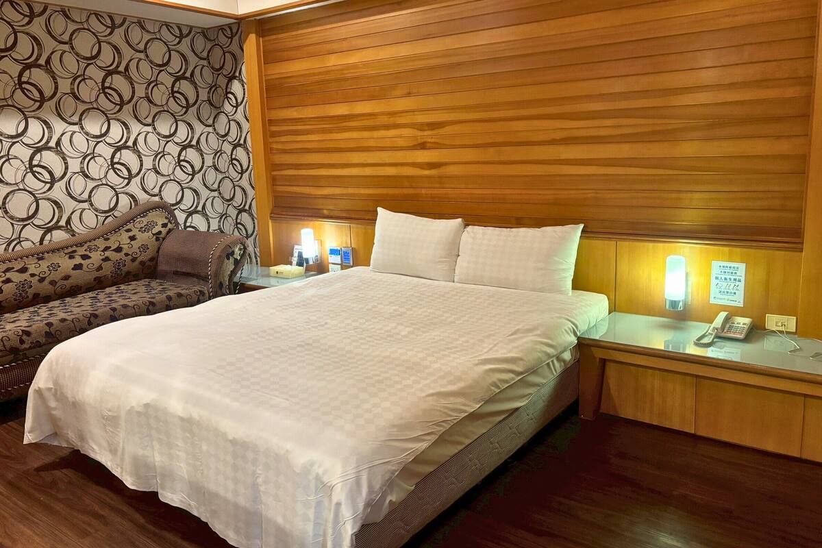 Una habitación de hotel con una cama grande, un sofá y una mesita de noche con un teléfono y una lámpara.