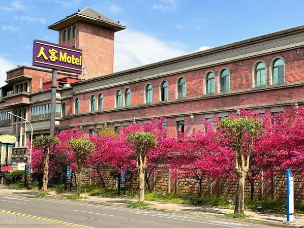 Un edificio de ladrillo con un cartel de hotel. Hay árboles con flores rosadas en el frente.