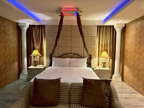 Una cama grande con dosel, dos mesitas de noche con lámparas y un sofá a rayas.