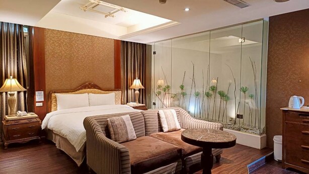 A modern hotel room with a large bed, a sofa, a small table, and a glass wall with plants. - Langkei Hotel (Taoyuan City)