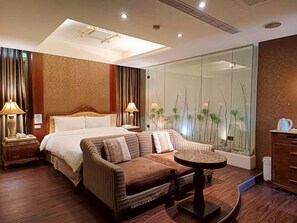 Una habitación de hotel moderna con una cama grande, un sofá, una mesita y una pared de vidrio con plantas.