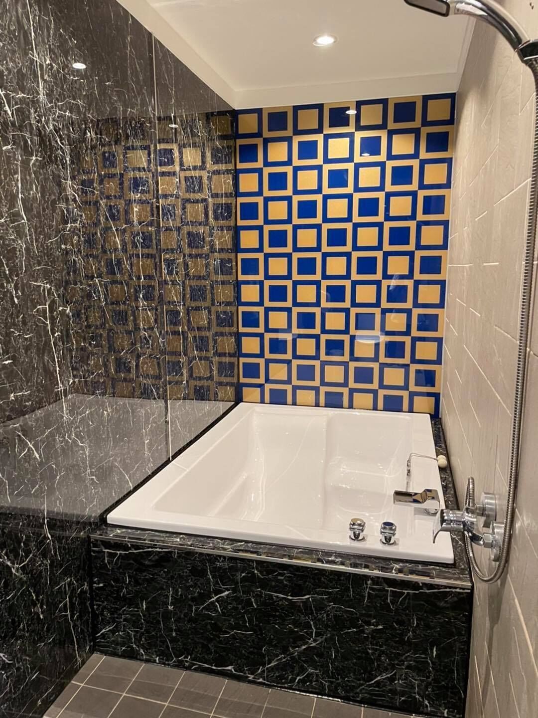 A modern bathroom with a marble floor, a white bathtub, and a shower area.