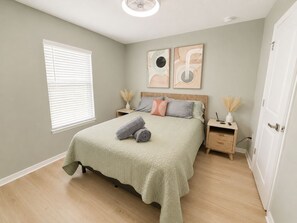 A bedroom with a bed, bedside tables, a window with blinds, and artwork on the wall.