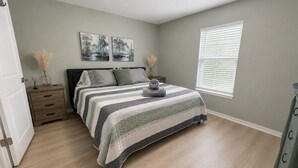 Un dormitorio con cama, mesita de noche, cómoda, ventana con persianas y decoración en la pared.