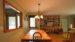Un coin repas avec une table et des bancs en bois, un lustre et une bibliothèque remplie de livres.