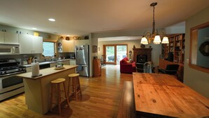 Une cuisine spacieuse avec un plancher en bois, un îlot central doté de tabourets, une table à manger et un coin salon confortable avec une cheminée.