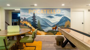 Een kamer met een muurschildering van een boslandschap, een pooltafel en een eethoek met stoelen en een tafel.