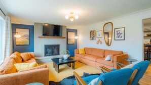 Een woonkamer met een open haard, oranje banken, een blauwe fauteuil en een salontafel.