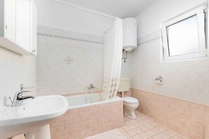 A bathroom with a bathtub, a sink, a toilet, and a window.